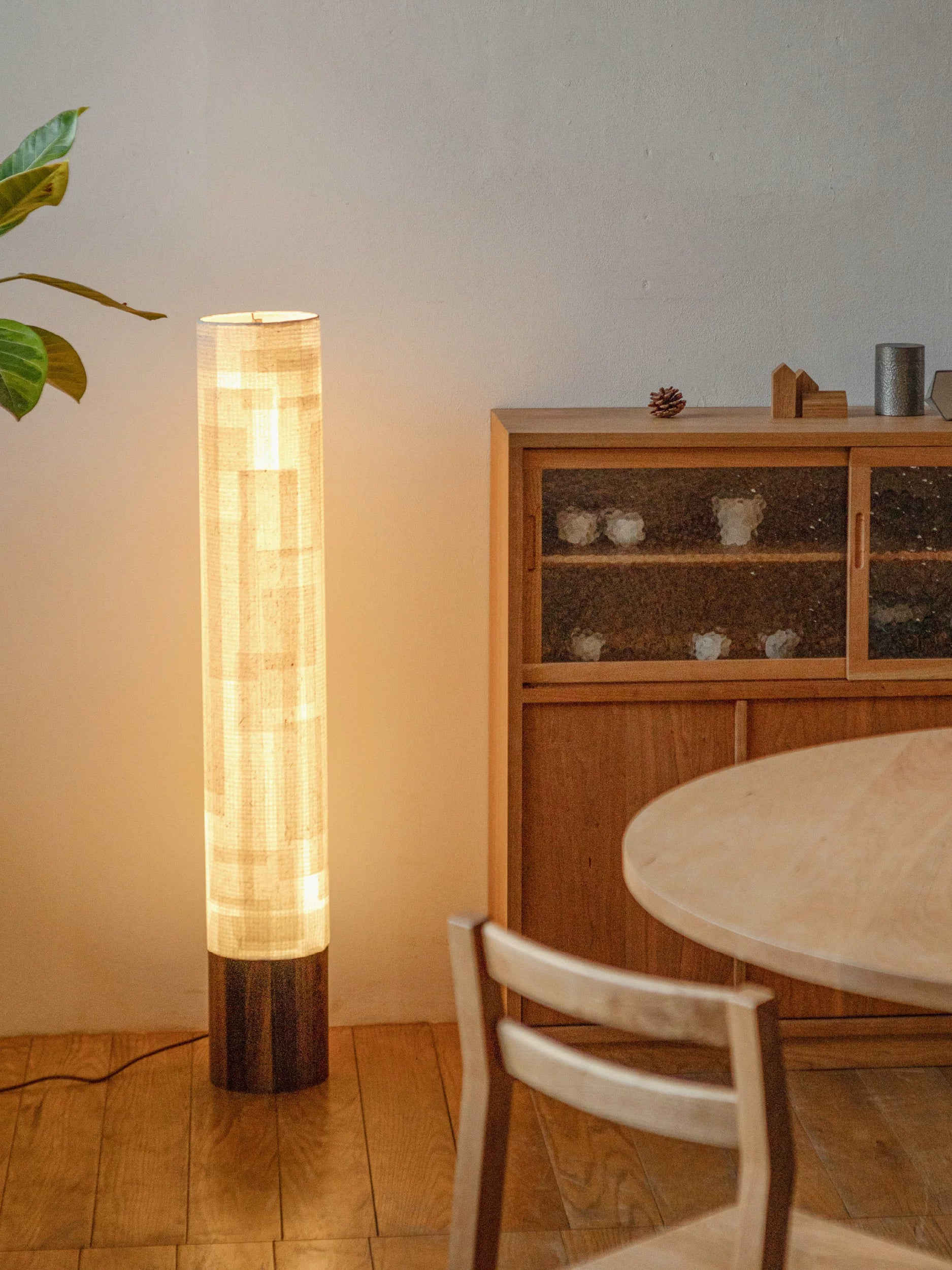 A tall paper floor lamp with a textured shade and a dark wood tripod base stands on a neutral floor.