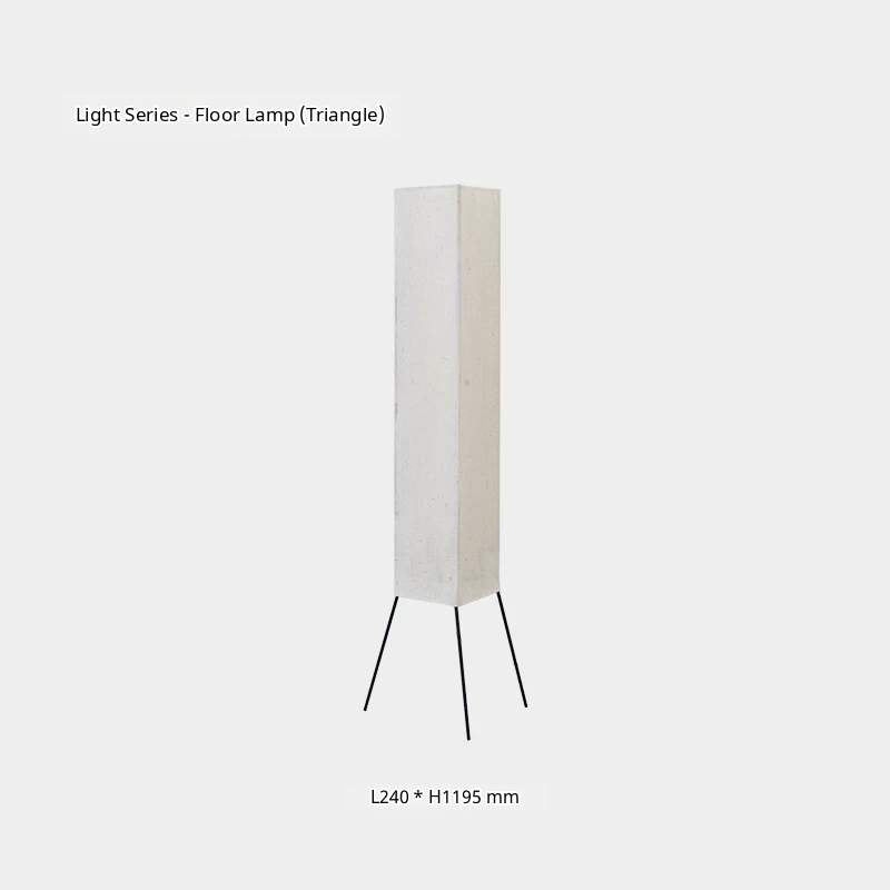 A cylindrical paper floor lamp with a wooden base stands on a wooden floor in a minimalist room.