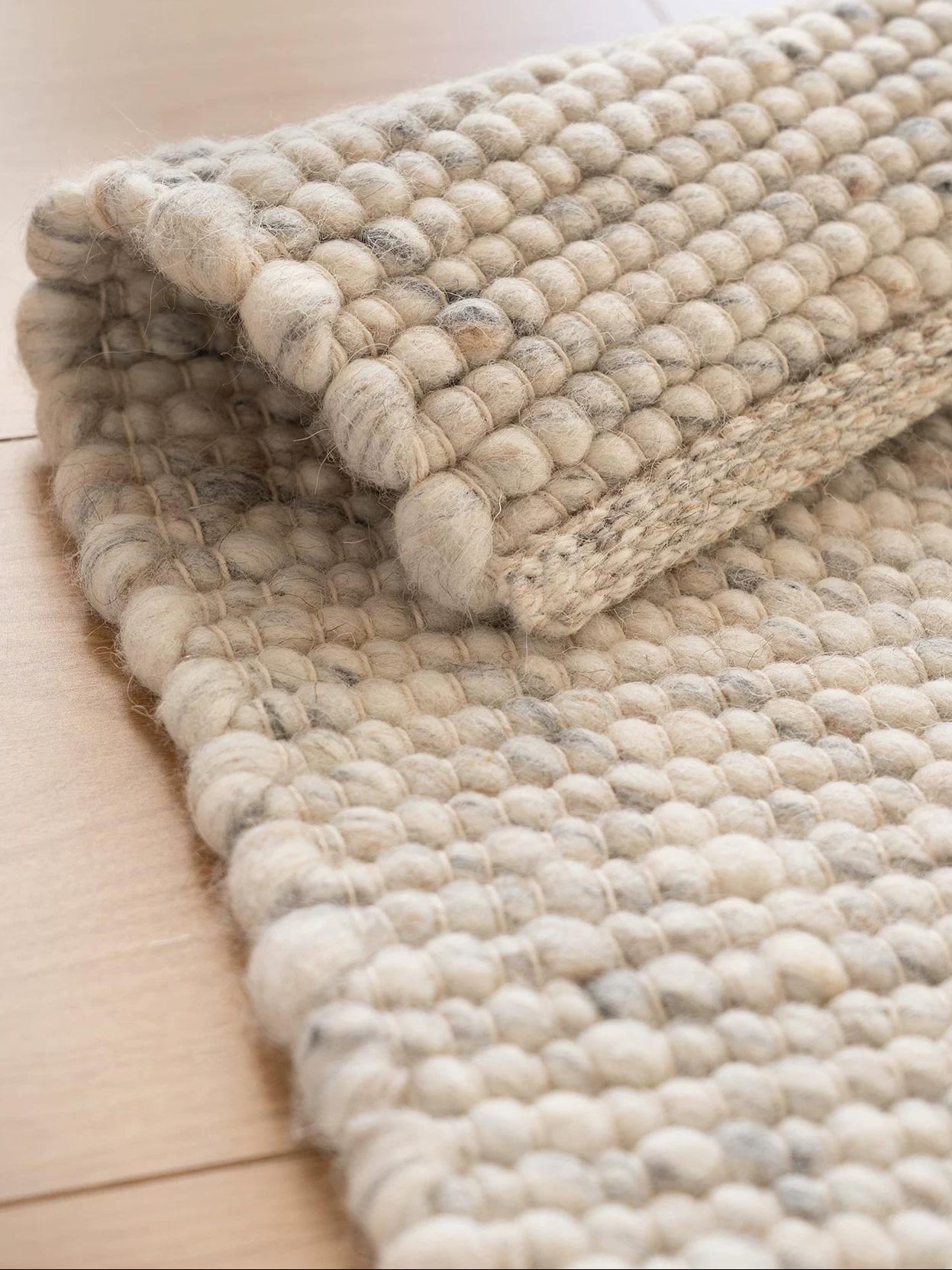 Cream wool rug with textured pebble weave rolled on wooden floor