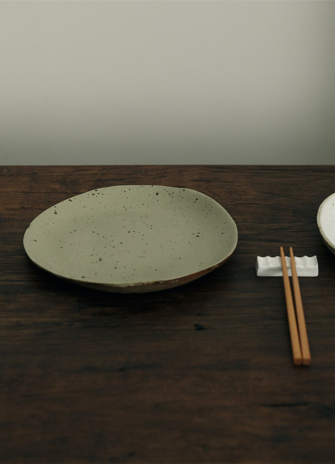 Earthenware dinner plate, speckled sage green, on dark wood table with chopsticks.