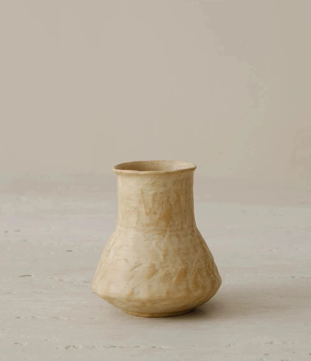 A small, hand-thrown ceramic vase with a textured, creamy white curd glaze and a rounded body.