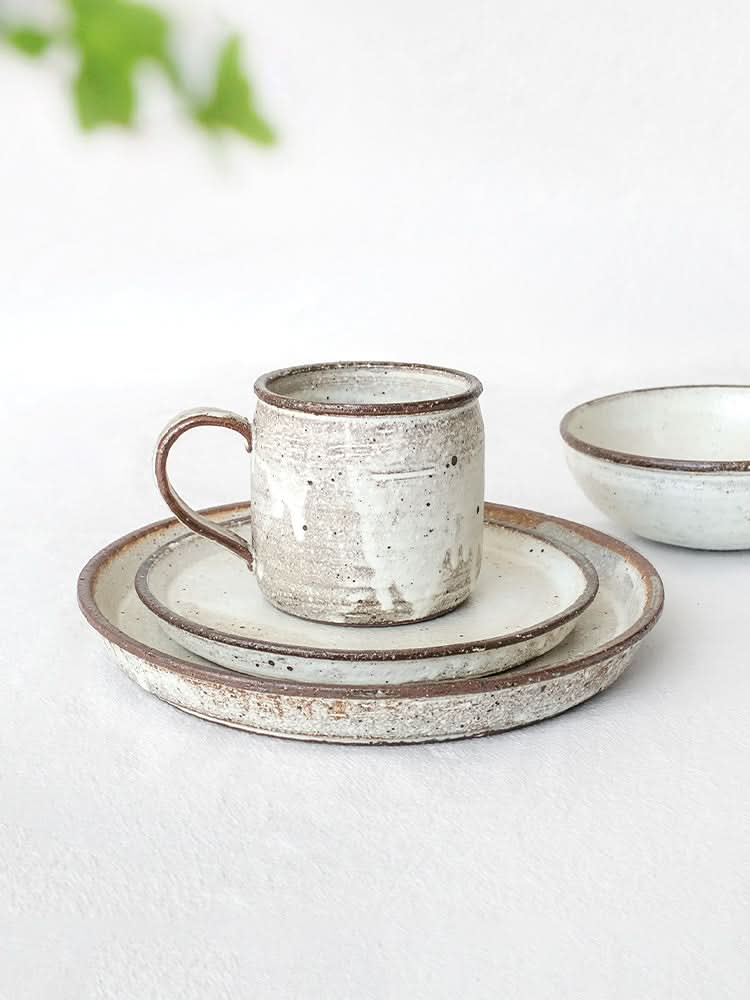 Clay ceramic white glazed dinnerware set with speckled texture and rustic brown rims.