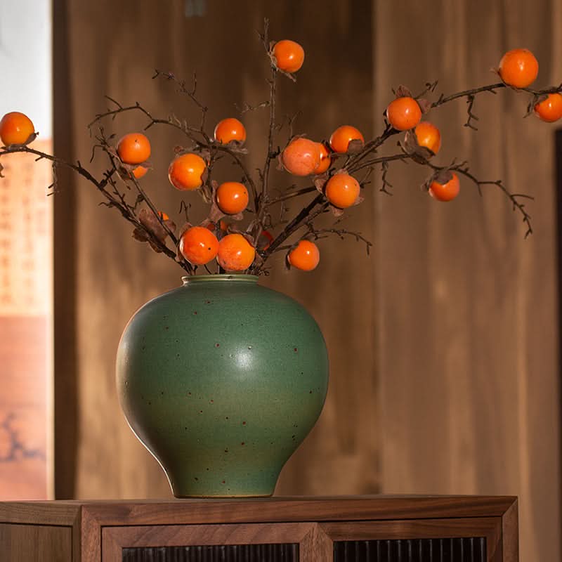 Sage Green Round Vase with persimmon branches on wooden surface. Home decor.
