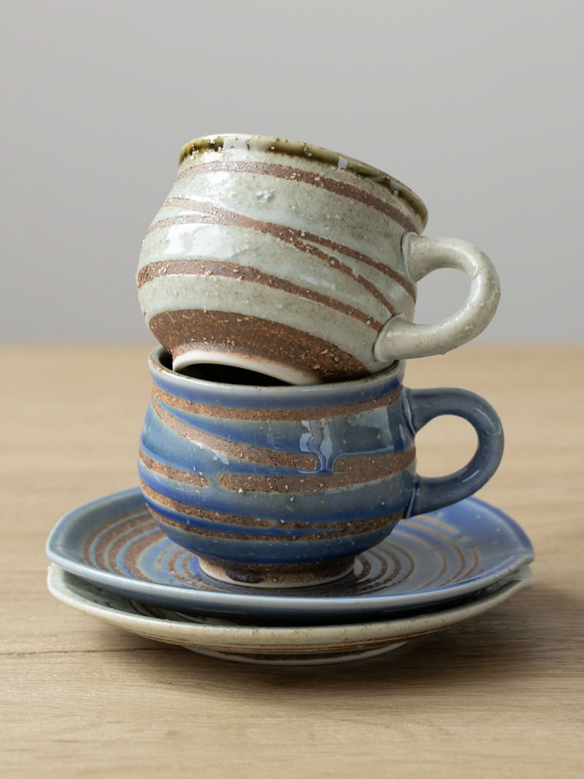 Two ceramic handmade mugs with coasters, blue and cream, with brown stripe glaze.