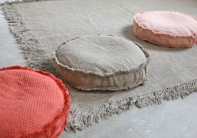 Round customizable textured floor cushion in natural, coral, & blush on woven rug.