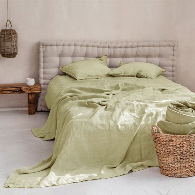 Soft olive green linen bed sheets, duvet, and pillows on a tufted headboard.