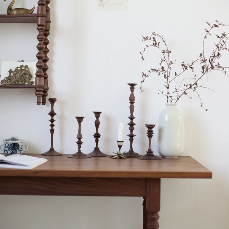Set of walnut wood pillar candle holders displayed on a wooden table with decorative branches in a vase.