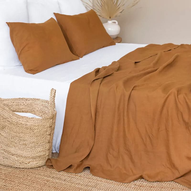 Caramel linen bed sheets with white base, two rust pillowcases, and a woven basket.
