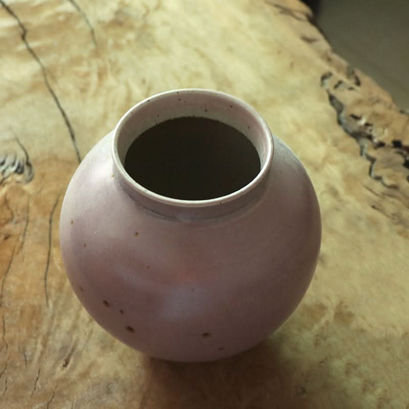 Handmade coarse pottery large round vase, light pink, textured wood background.