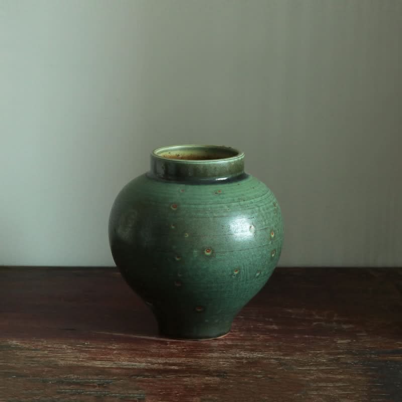 Handmade coarse pottery large round vase in deep green with subtle speckles, displayed on a wooden surface.