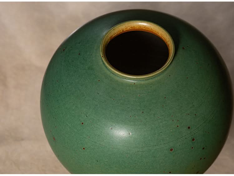 Sage green ceramic round vase with textured finish and rustic brown speckles.