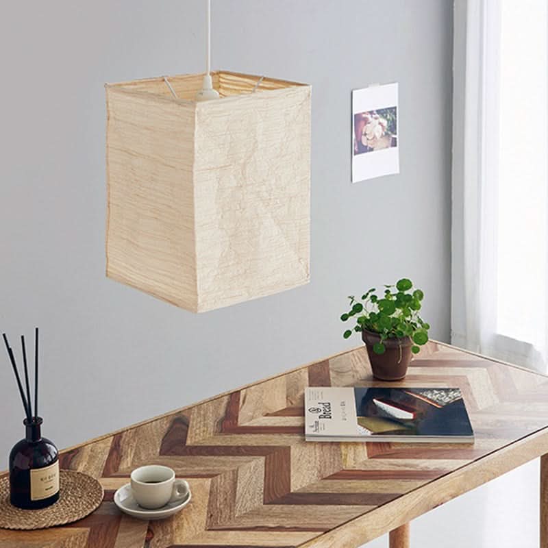 Natural fiber squared paper lampshade hanging over a wooden table with decor.