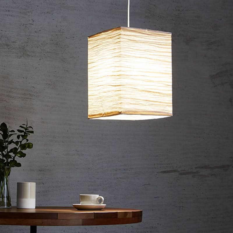 Textured squared paper lampshade with warm light, on a table with decor.