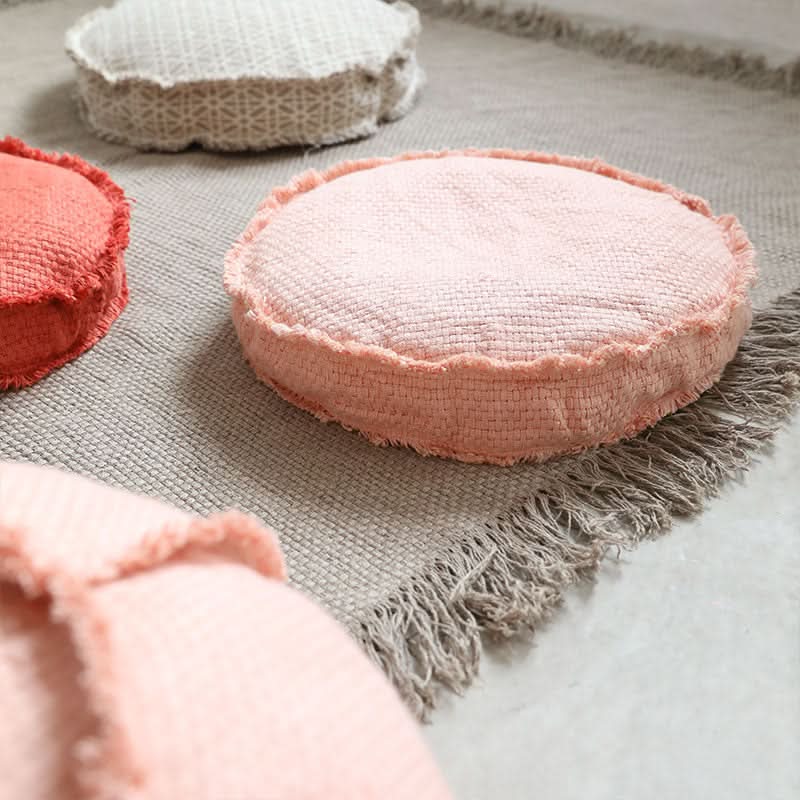 Round customizable textured floor cushion in pink, coral & beige on a fringed rug.