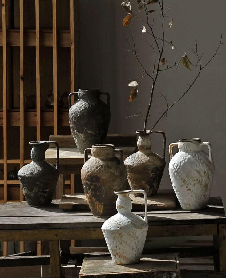 Assortment of rustic ceramic vases, including a wabi-sabi small ceramic vase, on a wooden table.