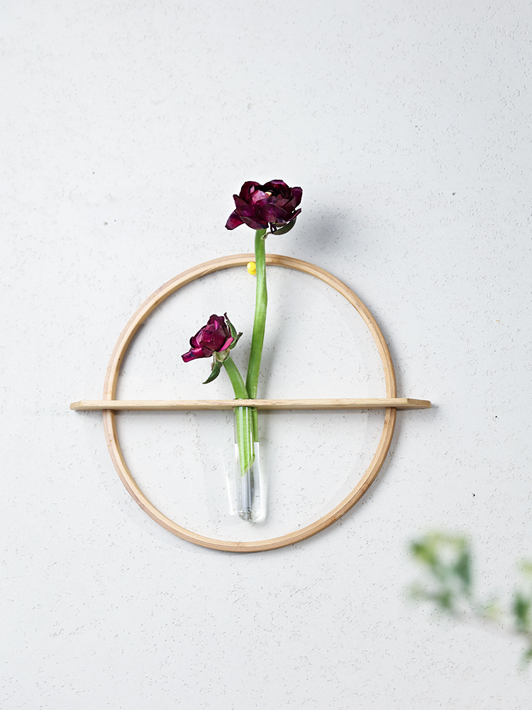 Wooden circular Wall Flower Vase with dark red flowers and glass vial, on a textured white wall.
