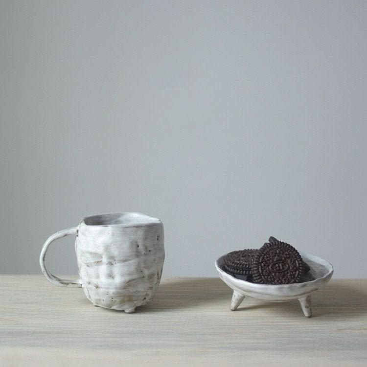 White textured stoneware mug with a small dish of cookies on a wooden surface. 2X1 Stoneware Mug Set.