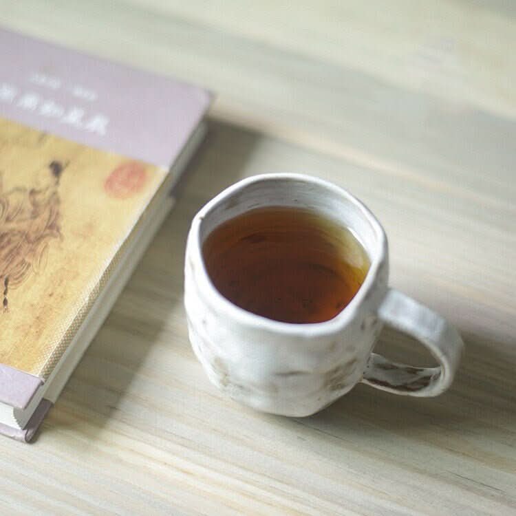 White textured 2X1 Stoneware Mug Set filled with tea, next to a book on a wooden surface.