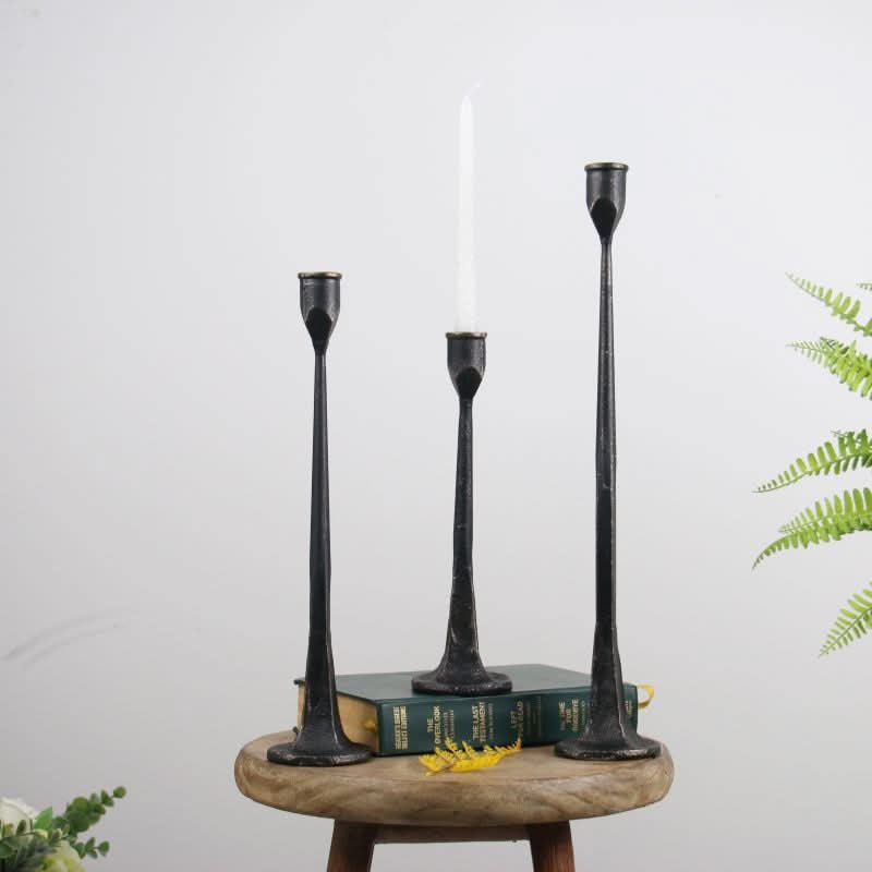Black iron candle holders in tall, slender design on wooden stool with books.