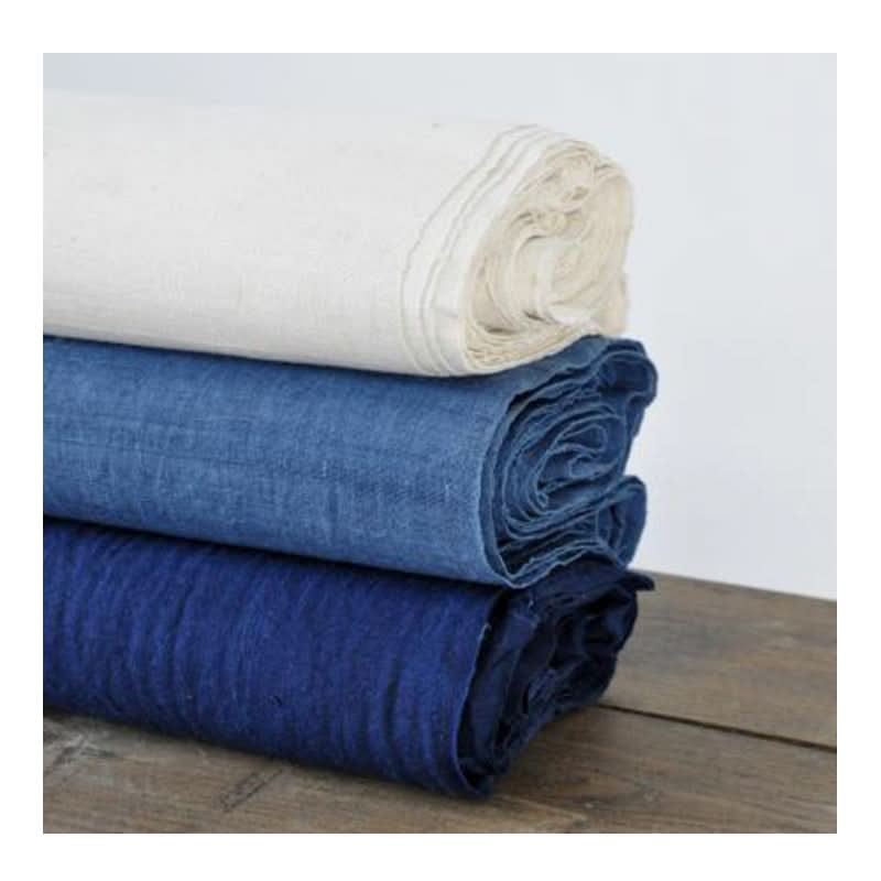 Stack of hand-woven native cotton fabrics in indigo and ecru tones, plant-dyed.