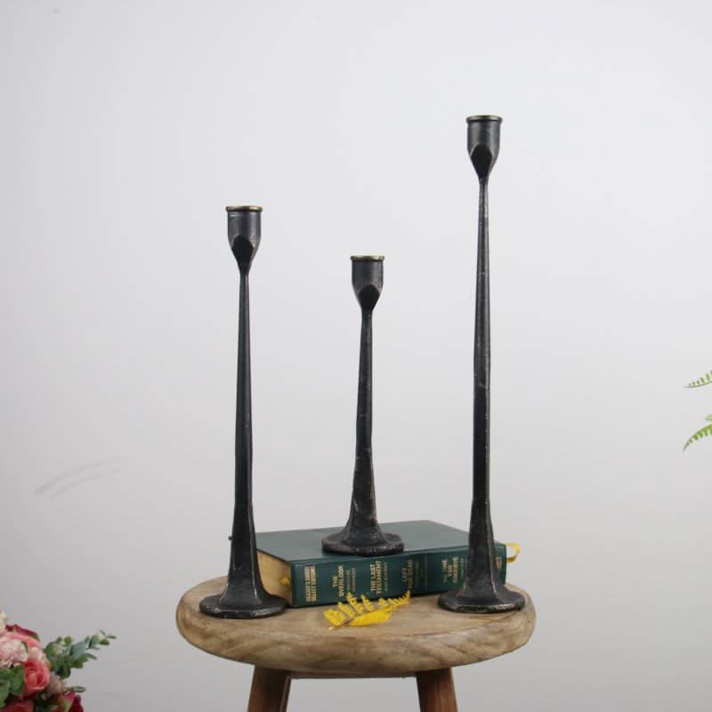 Black iron candle holders of varying heights on a wooden stool with books.