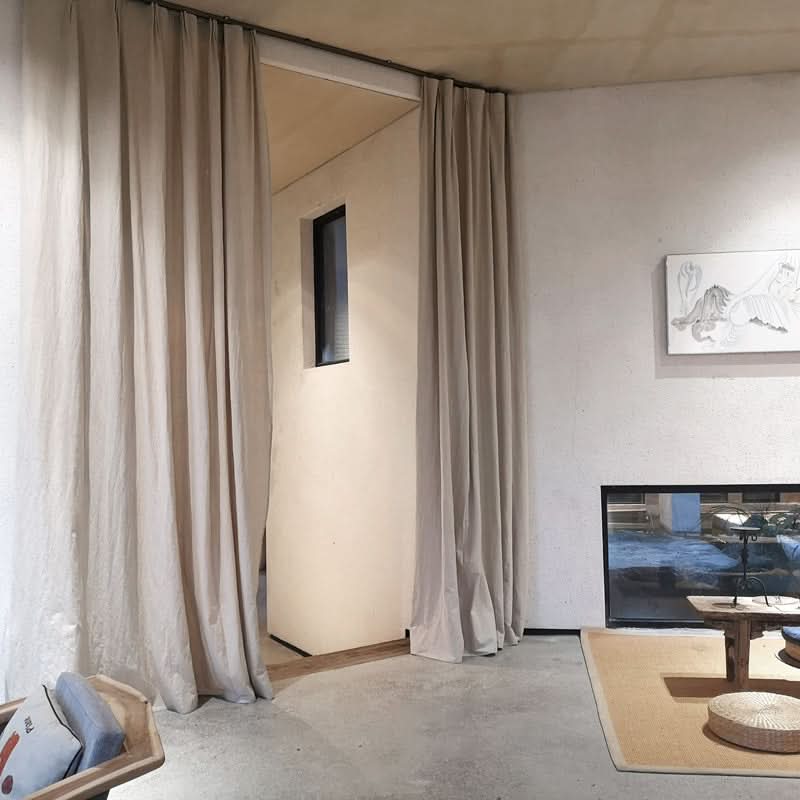 Cream linen curtains frame a doorway with a minimalist interior, showcasing natural texture.