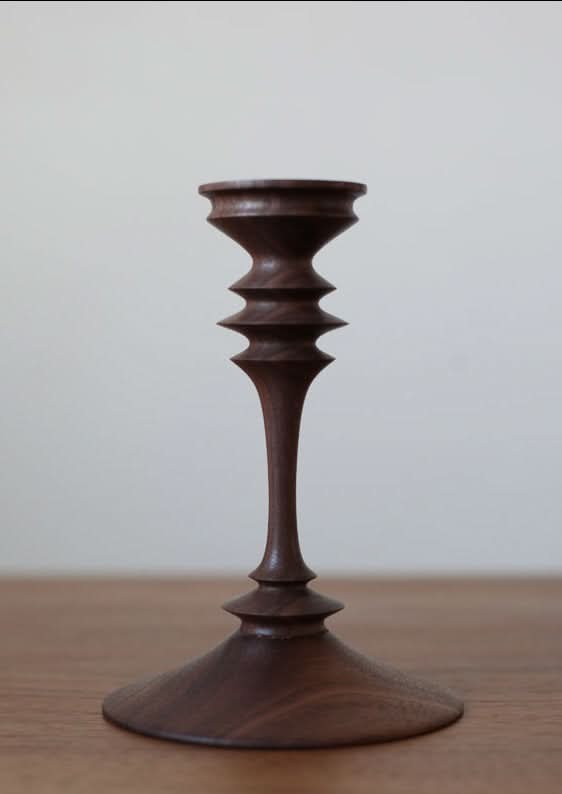 Walnut wood pillar candle holder with sculpted detail on a wooden surface.