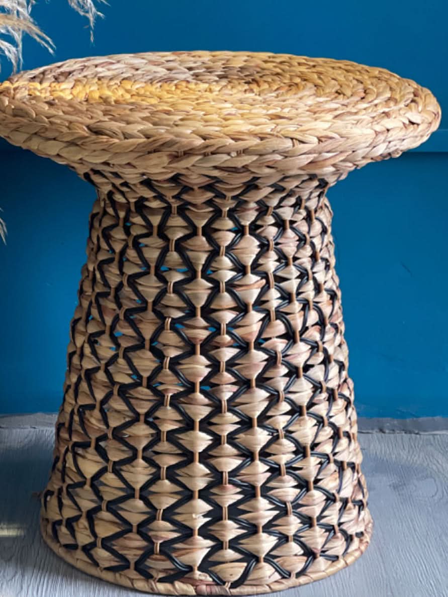 Natural woven Wabi Sabi coffee table straw with dark accents against blue wall.