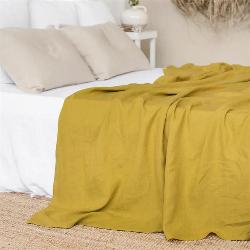 Mustard yellow linen bed sheets draped on a white bed, with neutral pillows.