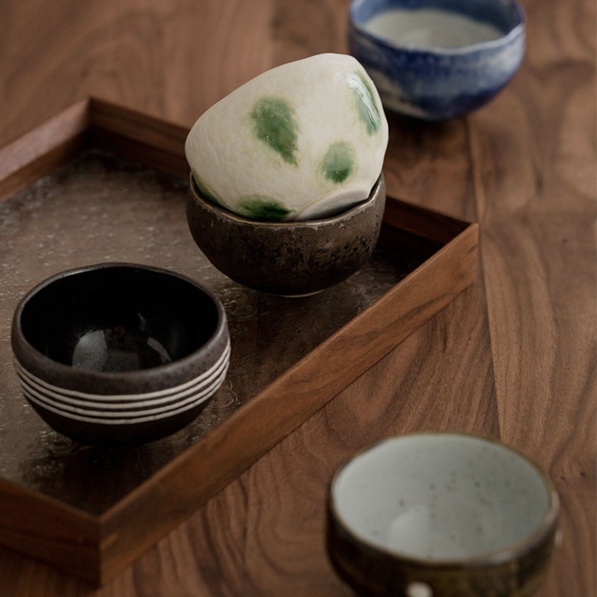 Japanese tea set with ceramic bowls on a wooden tray, featuring earthy tones and subtle green accents.