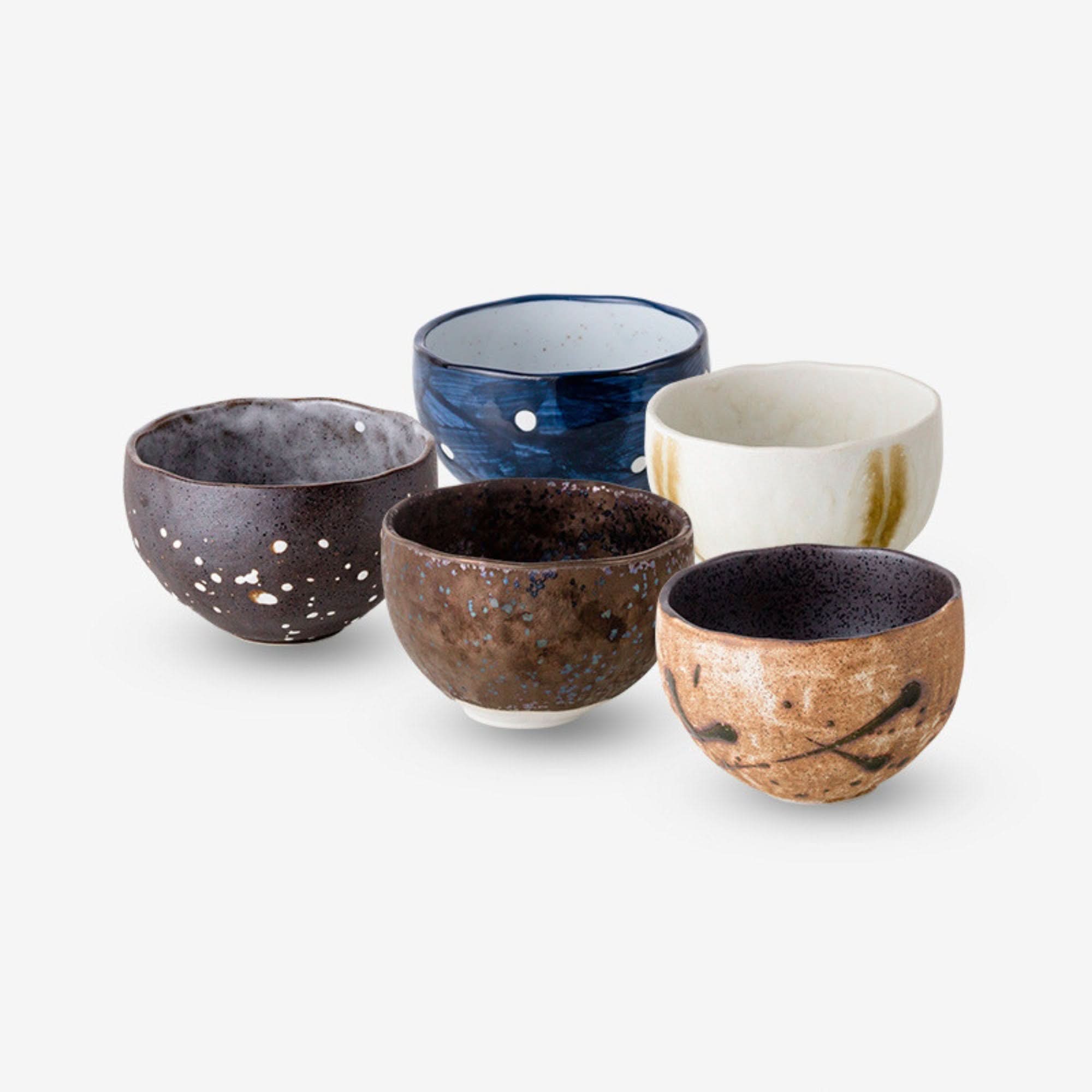 Assorted ceramic Japanese tea set cups: speckled dark, blue splatter, white/gold, brown speckled, and textured brown.