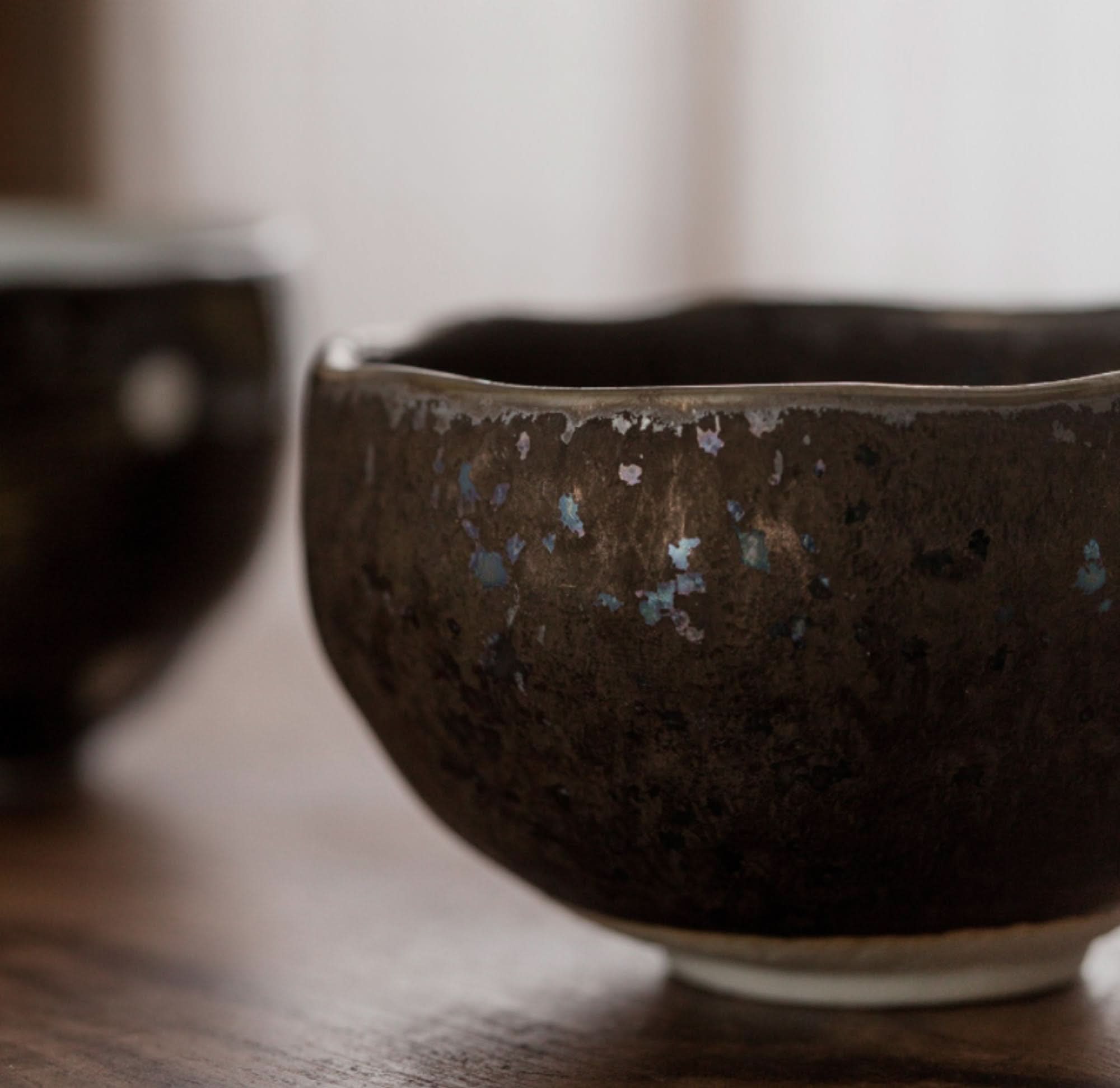 Dark brown ceramic tea cup with blue flecks, part of a Japanese tea set.
