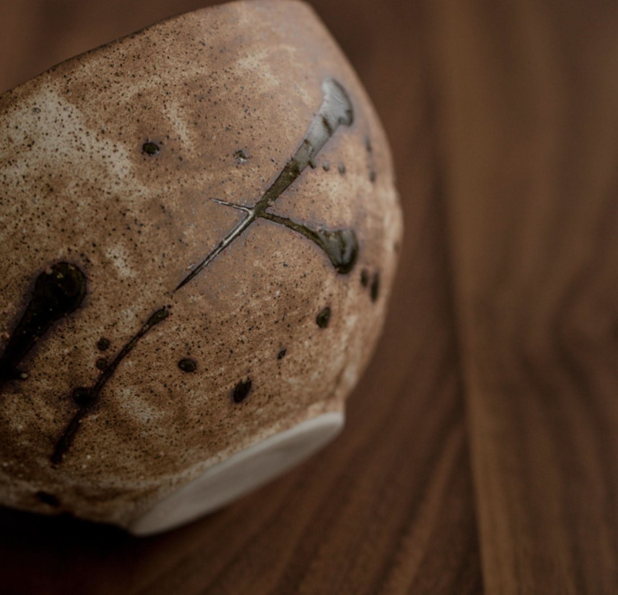 Brown ceramic Japanese tea set cup with speckled texture and dark glaze accents on a wooden surface.