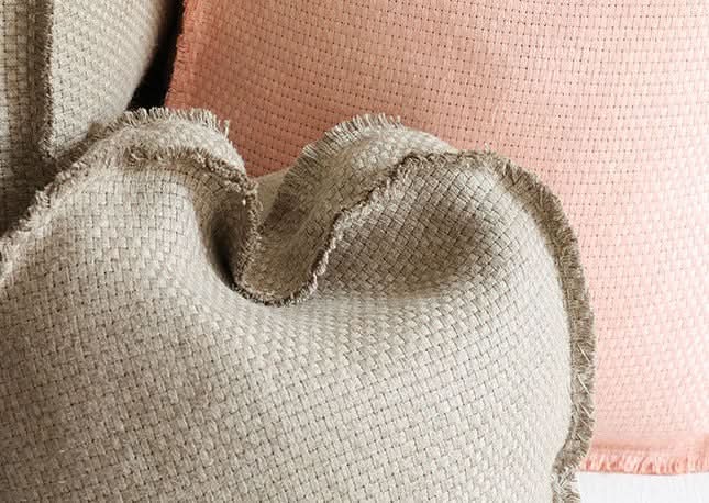 Close-up of beige textured floor cushion with frayed edge, beside pink home decor textile.