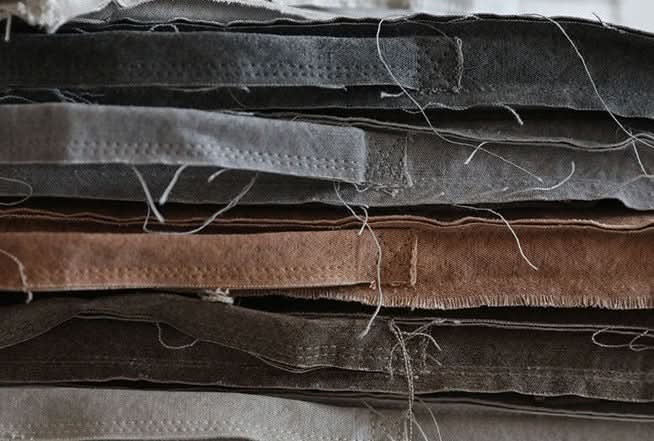 Stack of customizable distressed linen cushion fabrics in grey and brown tones.