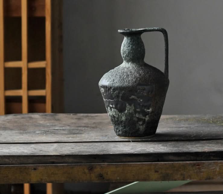 Wabi-sabi small ceramic vase with textured dark glaze on rustic wooden table.
