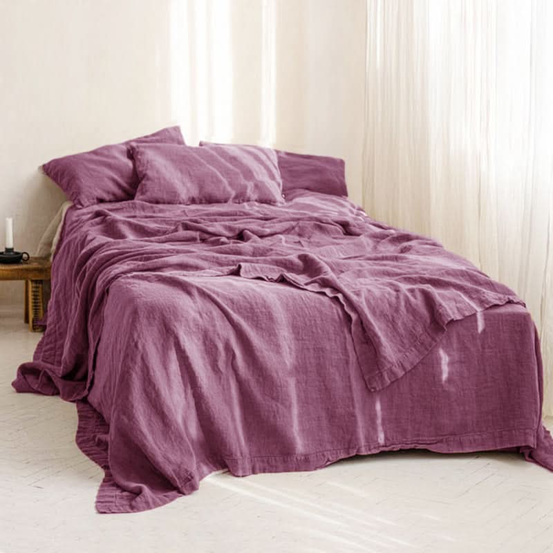 Plum linen bed sheets with a relaxed drape on a made bed.