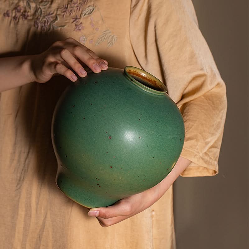 Sage green ceramic round vase, textured, held by hands.