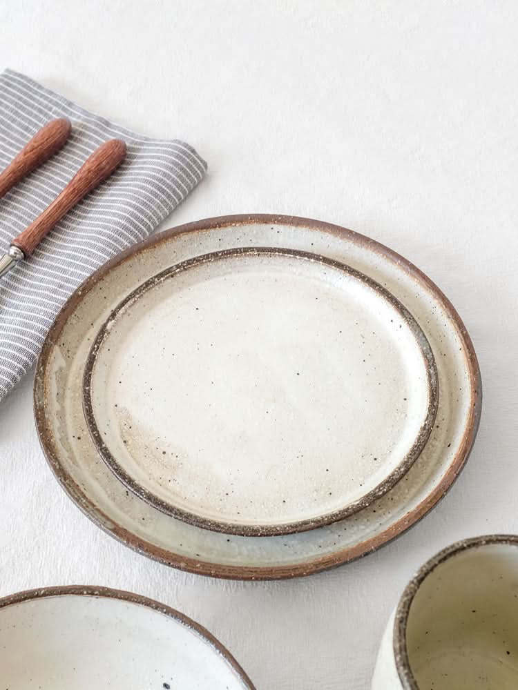 White glazed ceramic dinnerware set with rustic brown edges, on a striped cloth.
