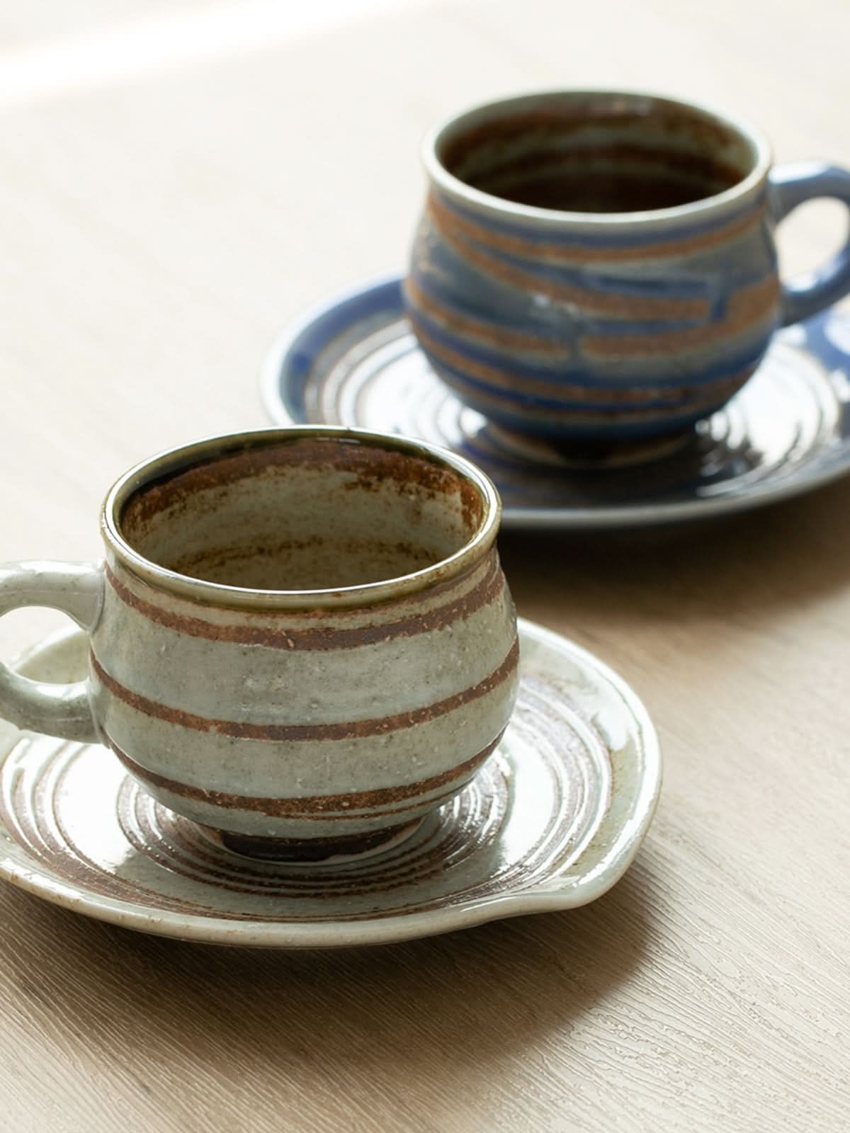 Ceramic handmade mug with coaster, rustic earth tones with blue accents.