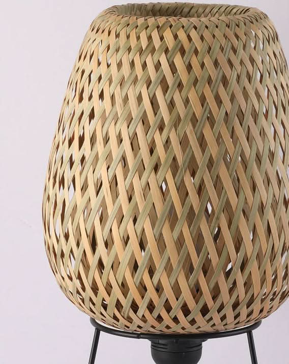 Woven natural rattan table lamp with a textured, earthy design on a black metal base.
