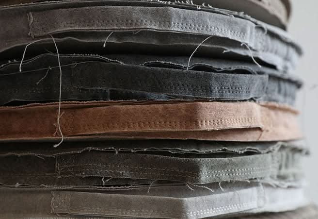 Stack of customizable distressed linen cushion covers in grey, taupe, and dark grey.