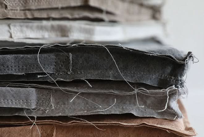 Stacked gray & taupe customizable distressed linen cushions with loose threads.