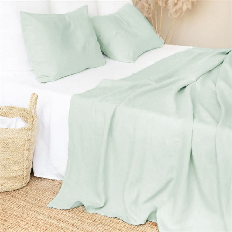 Pale green linen bed sheets and pillowcases on a bed, with a woven basket.