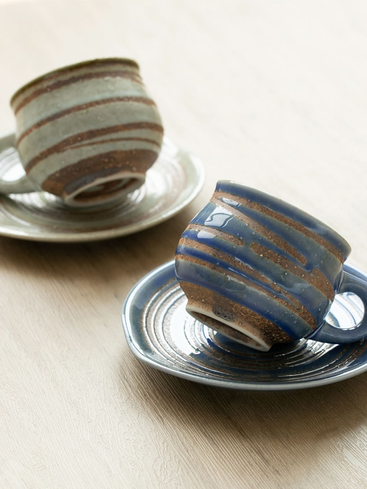 Ceramic handmade mug with coaster, blue and grey swirl design, on a wooden surface.
