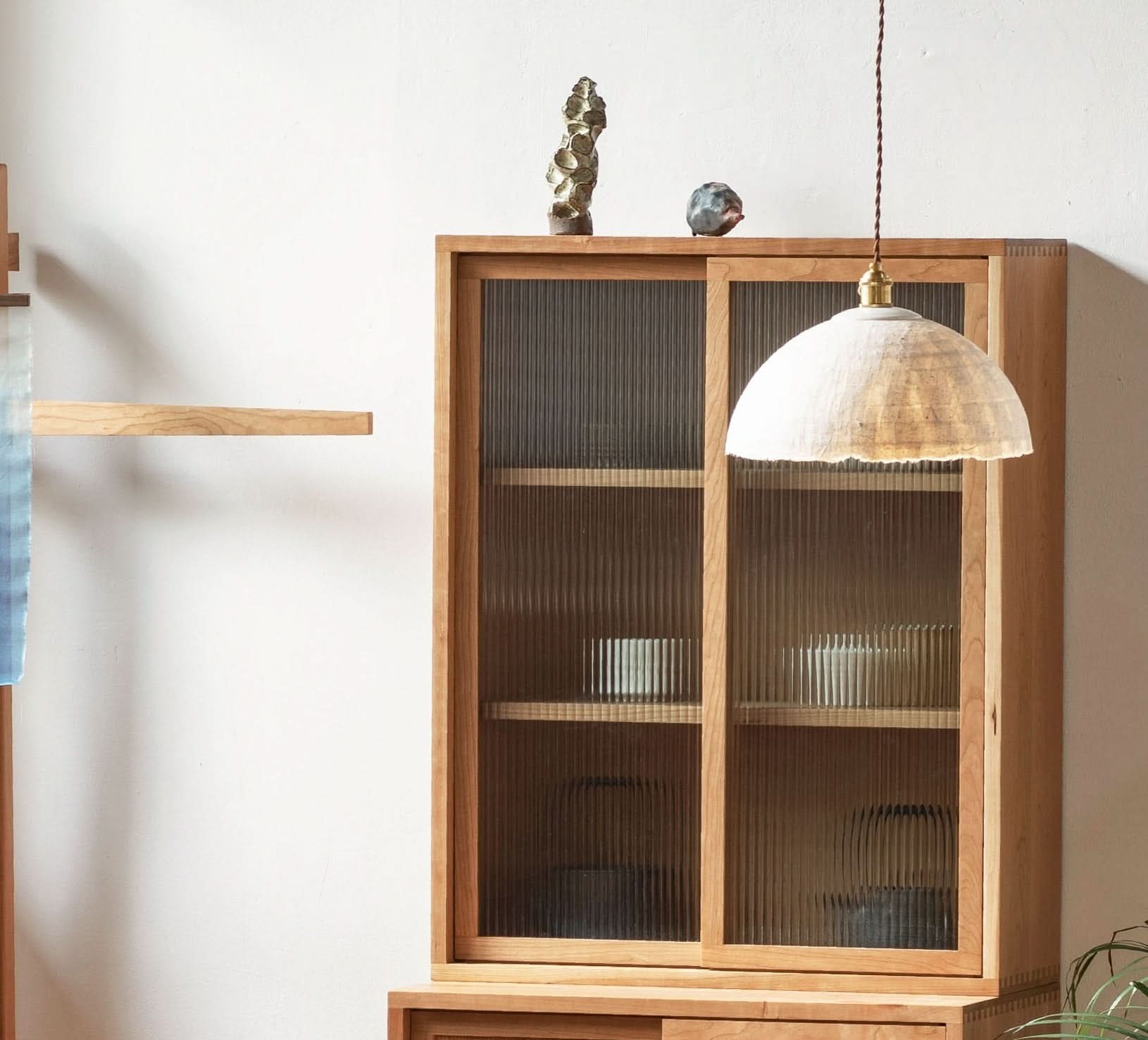Textured white paper mache lamp shade hanging over a wooden cabinet in a cozy home decor setting.