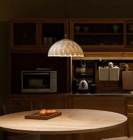 Natural paper mache lamp shade hanging in a warm, modern kitchen setting.