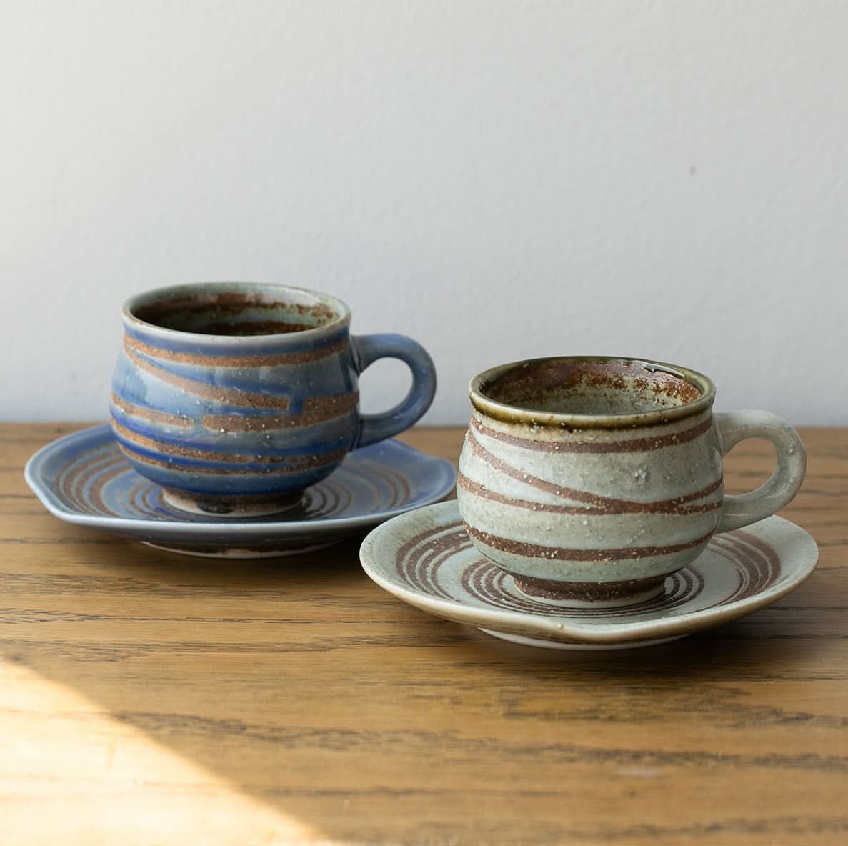 Ceramic handmade mug with coaster in blue and earth tones, on a wooden table.