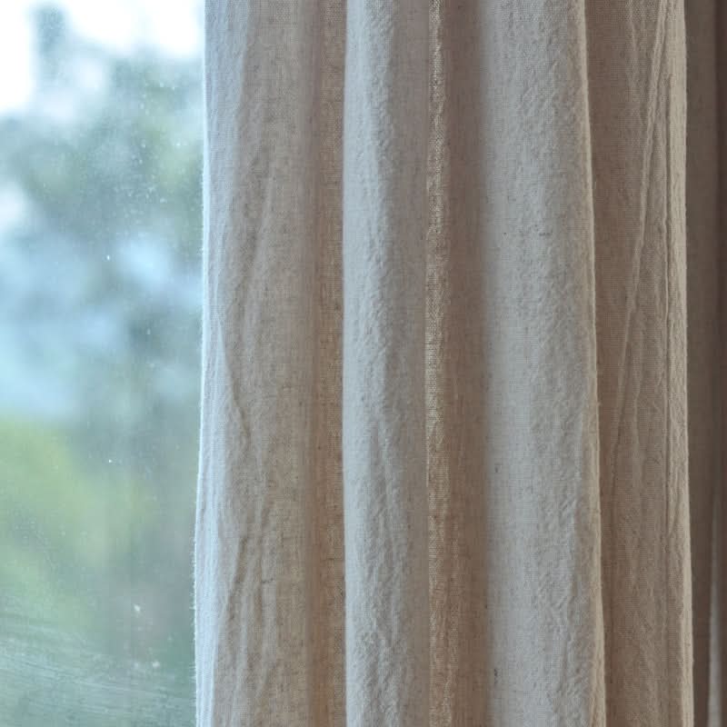Cream linen curtains drape across a window, letting in diffused natural light.