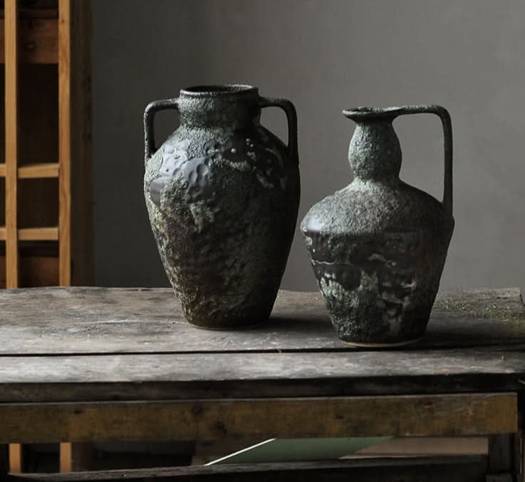 Two rustic Wabi-sabi small ceramic vases with textured dark glaze on a wooden surface.
